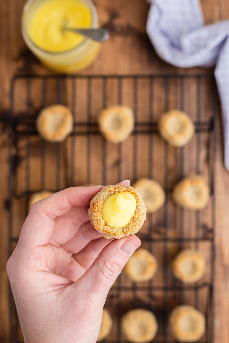 Overhead photo of Keto Lemon Thumbprint Cookies cooling on a rack with one filled with lemon curd closer to the camera.