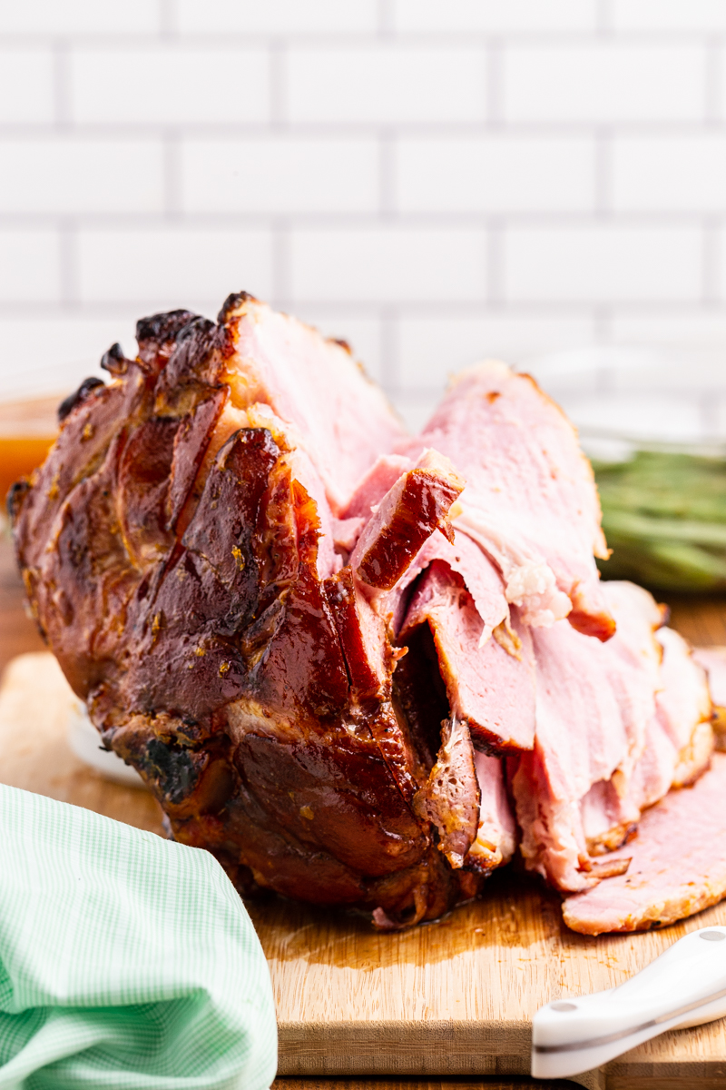 Photo of Keto Apricot Bourbon Glazed Ham on a cutting board with green beans in the background.