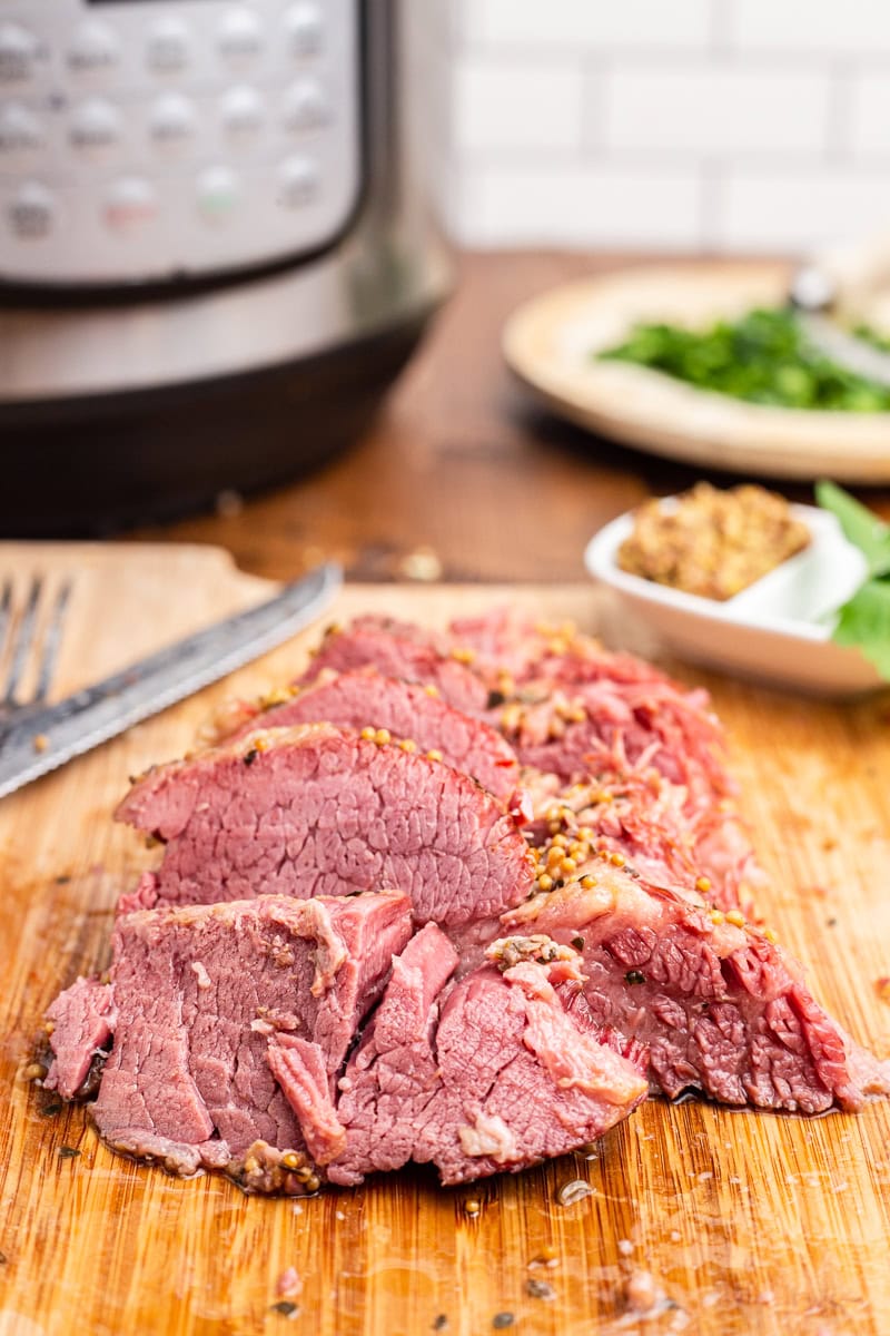 Keto corned beef on a wooden cutting board with an instant pot in the background.