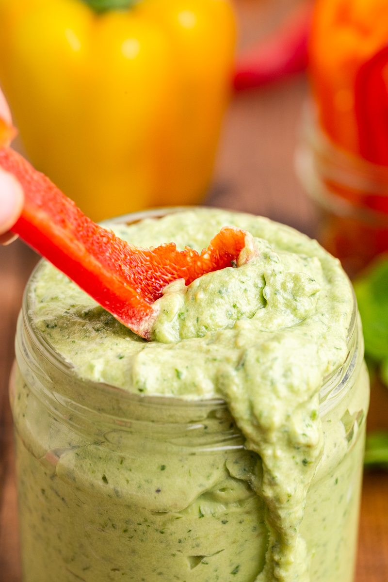 Avocado Ranch Dip in a mason jar with someone scooping some out with a bell pepper slice.