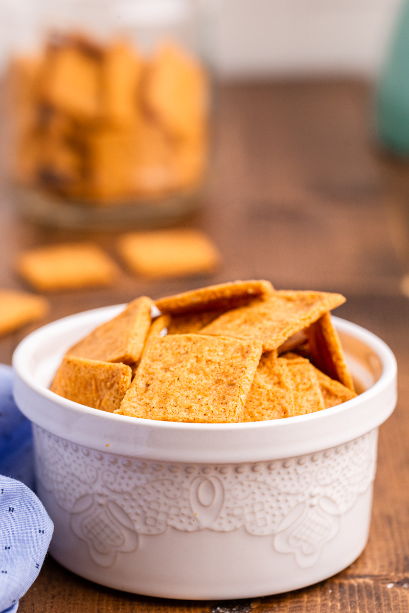 Photo of Keto Smoked Cheddar Crackers (Cheez-Its) in a white bowl on a wooden table.