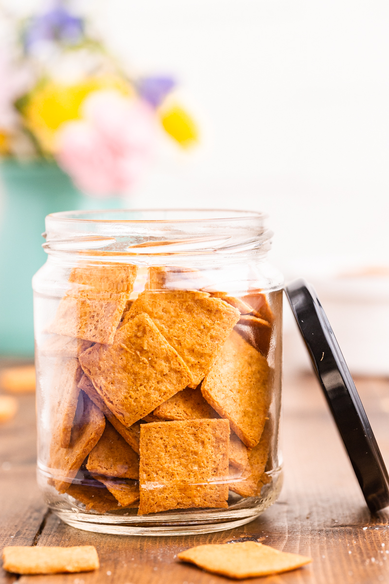 Photo of Keto Smoked Cheddar Crackers (Cheez-Its)  in a glass jar on a wooden table with the sun shining on it.