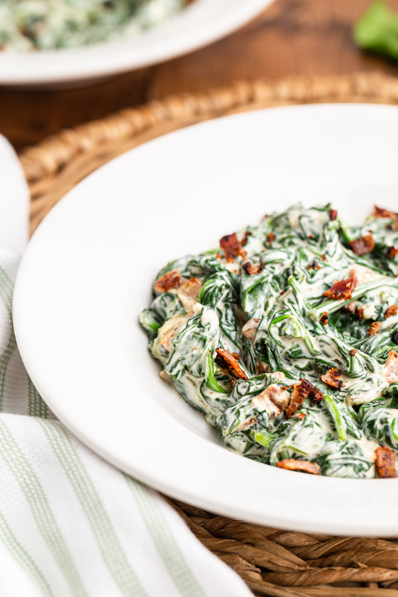 Closeup photo of a serving of Easy Creamed Spinach in a white bowl on a wooden table.