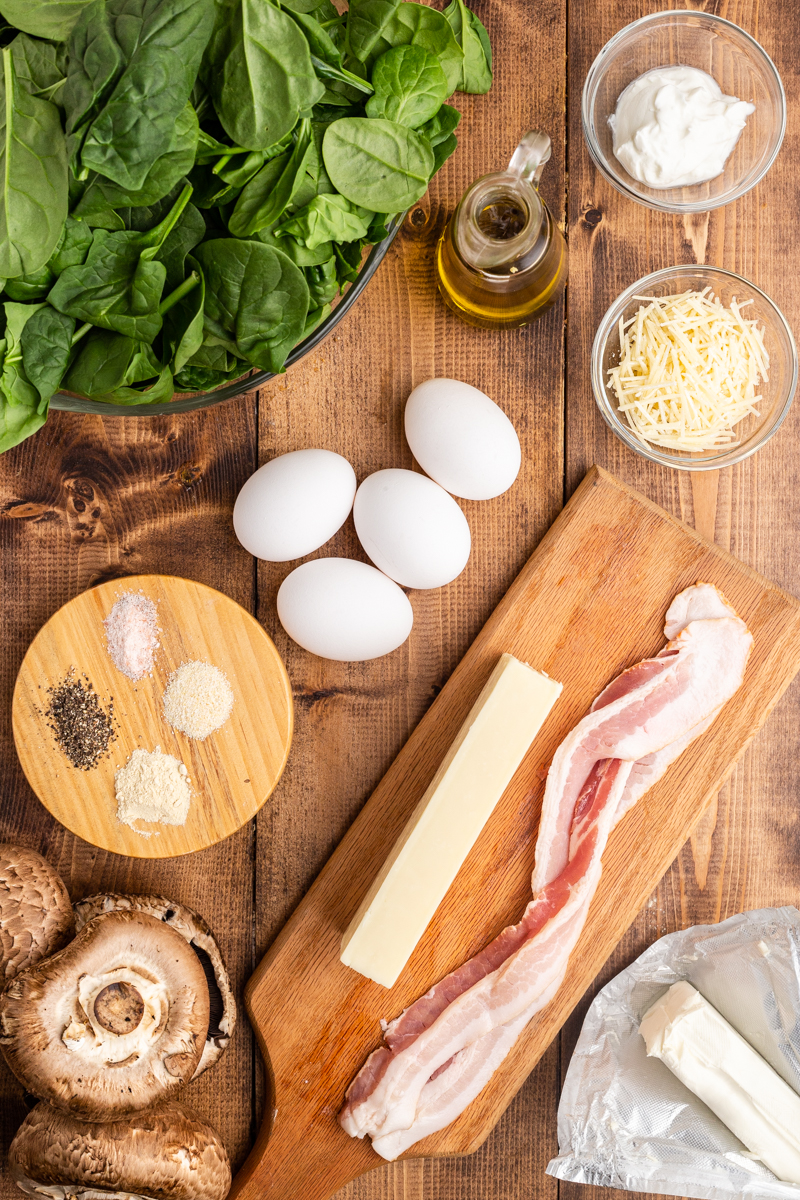 Photo of the ingredients needed to make Keto Spinach and Egg Stuffed Mushrooms on a wooden table.