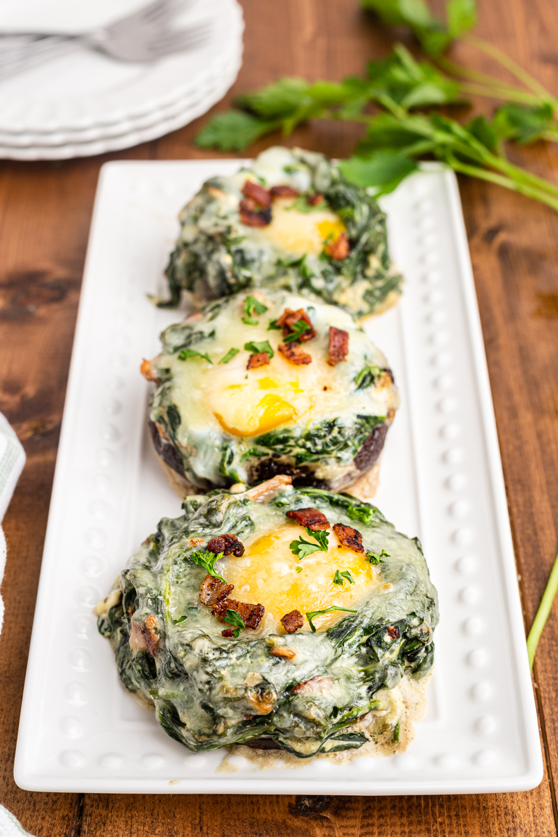 Photo of three Keto Spinach and Egg Stuffed Mushrooms on a white platter.