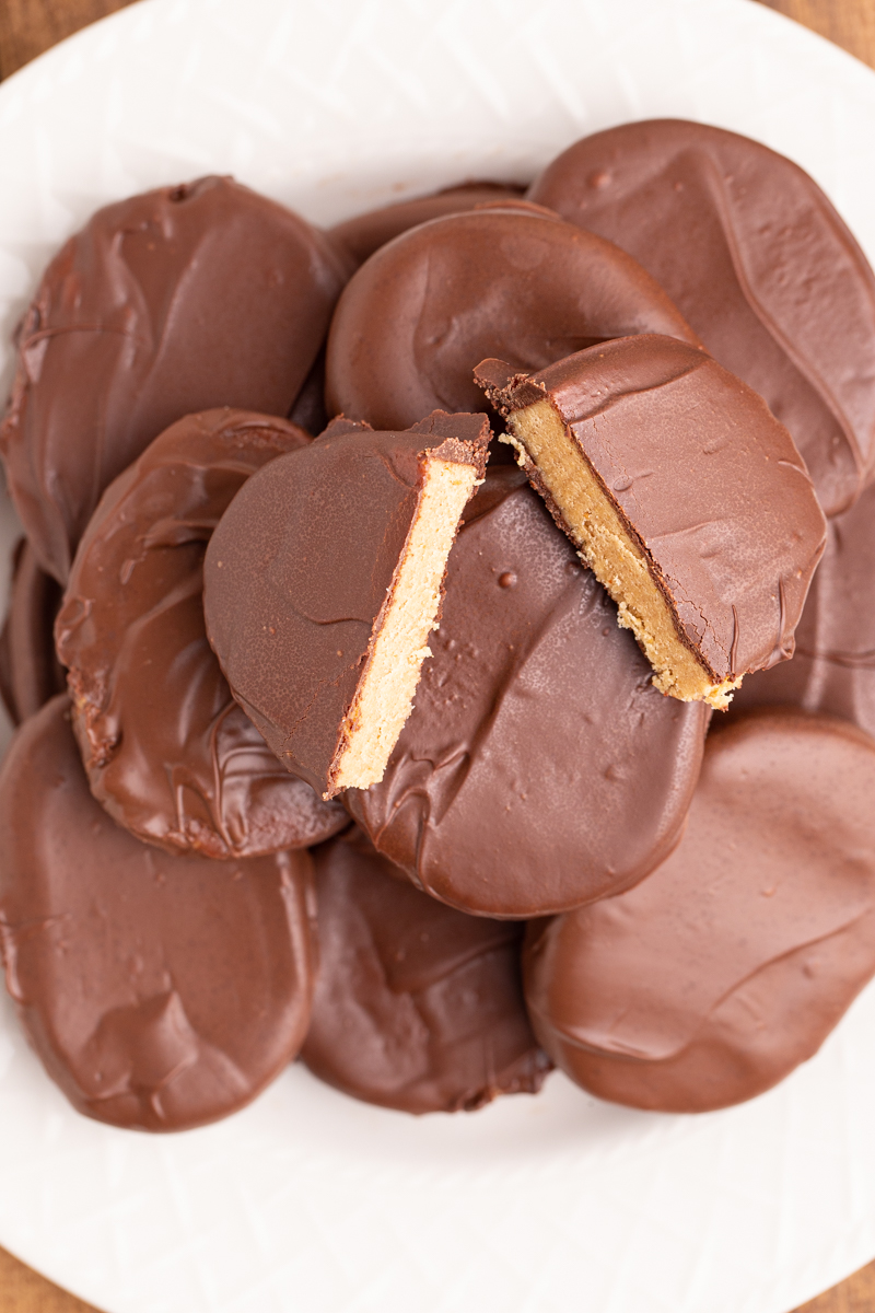 Overhead photo of several Keto Peanut Butter Chocolate Easter Eggs on a white plate with one egg cut in half so you can see the peanut butter inside.