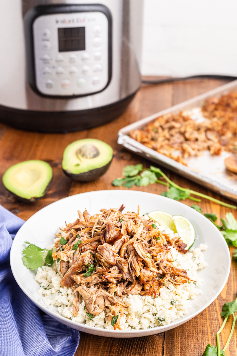 Photo of a burrito bowl made with Easy Keto Pork Carnitas on a wooden table with an Instant Pot in the background.