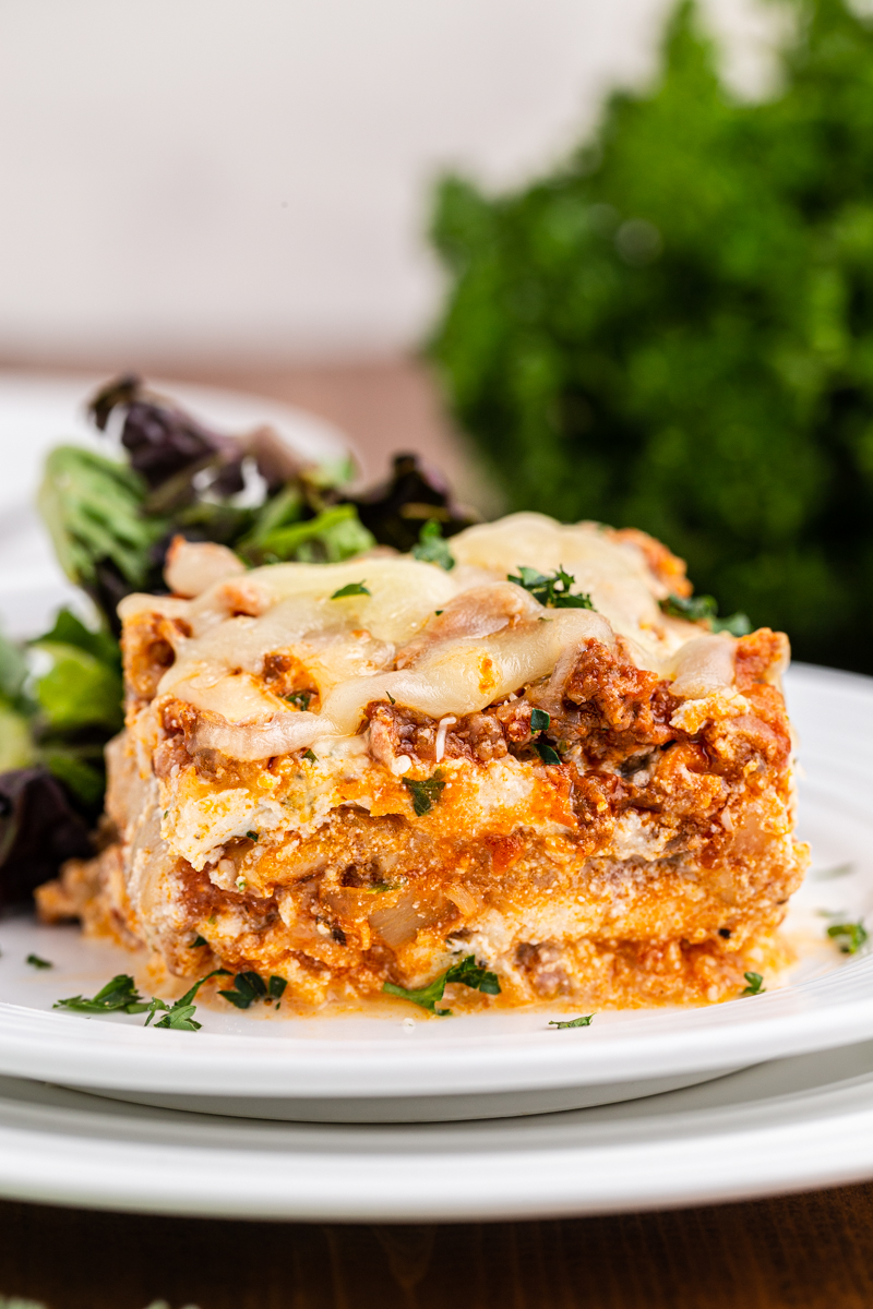 Close up photo of a serving of keto lasagna on a white plate with a salad.