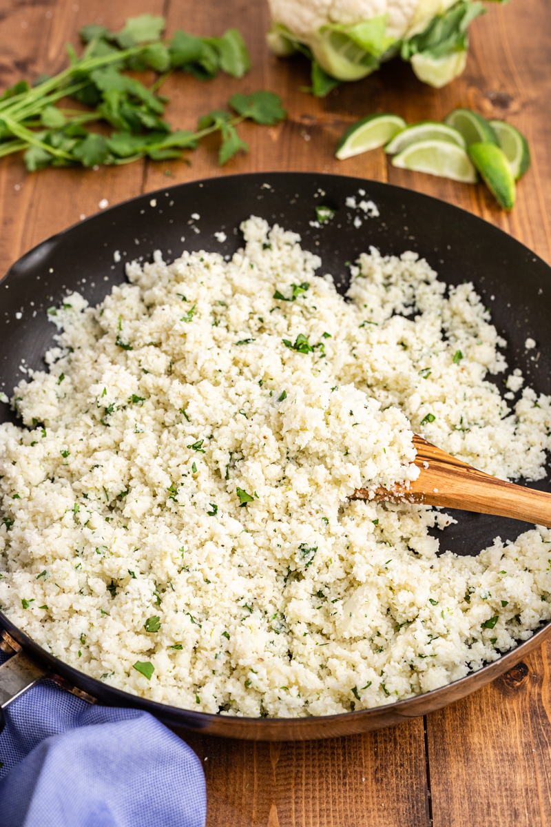 Photo of a skillet with Copycat Chipotle Cilantro Lime Cauliflower Rice in it on a wooden table.