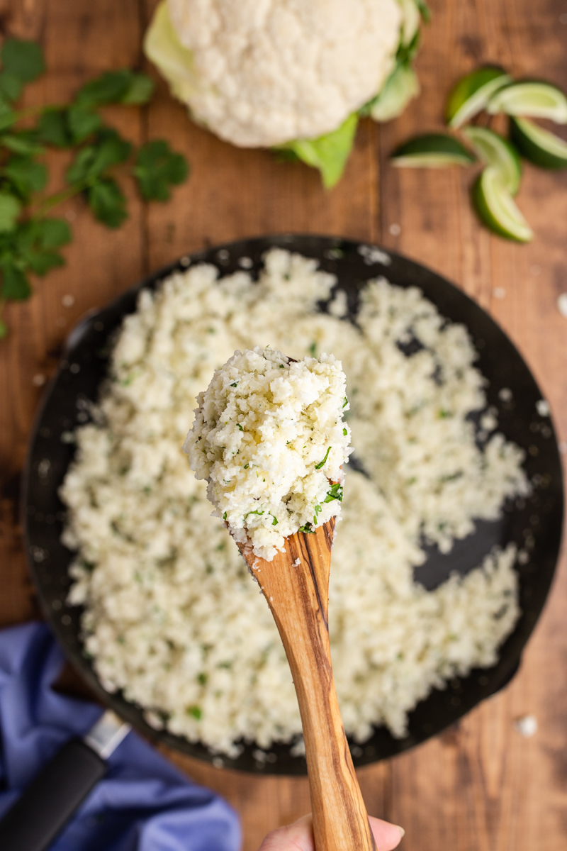Overhead photo of Copycat Chipotle Cilantro Lime Cauliflower Rice in a skillet with a wooden spoonful closer to the camera.