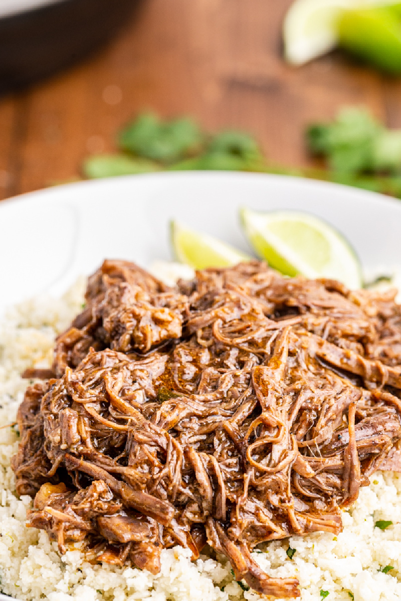 Closeup photo of Instant Pot Mexican Shredded Beef  (Keto, Paleo, Gluten-free) in white bowl with cilantro lime cauliflower rice and lime wedges.