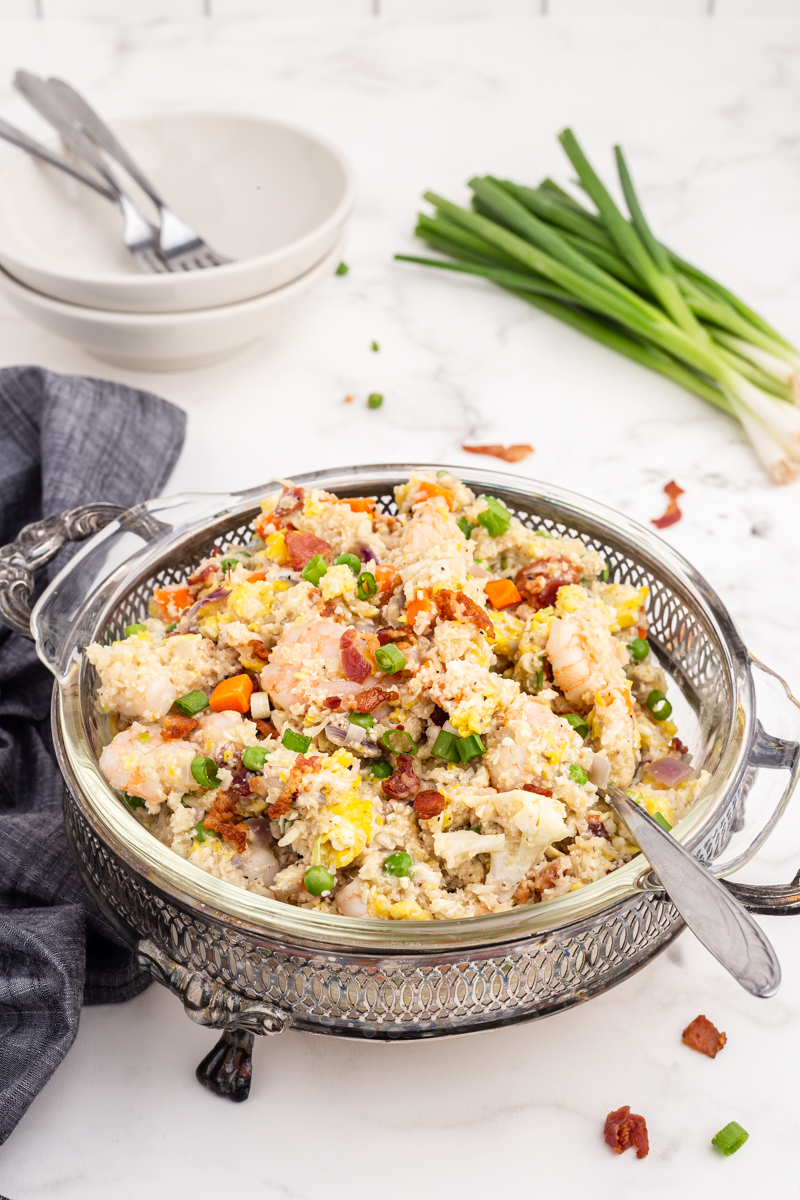 Shrimp Fried Cauliflower Rice with Bacon in a glass serving dish on a white marble counter.