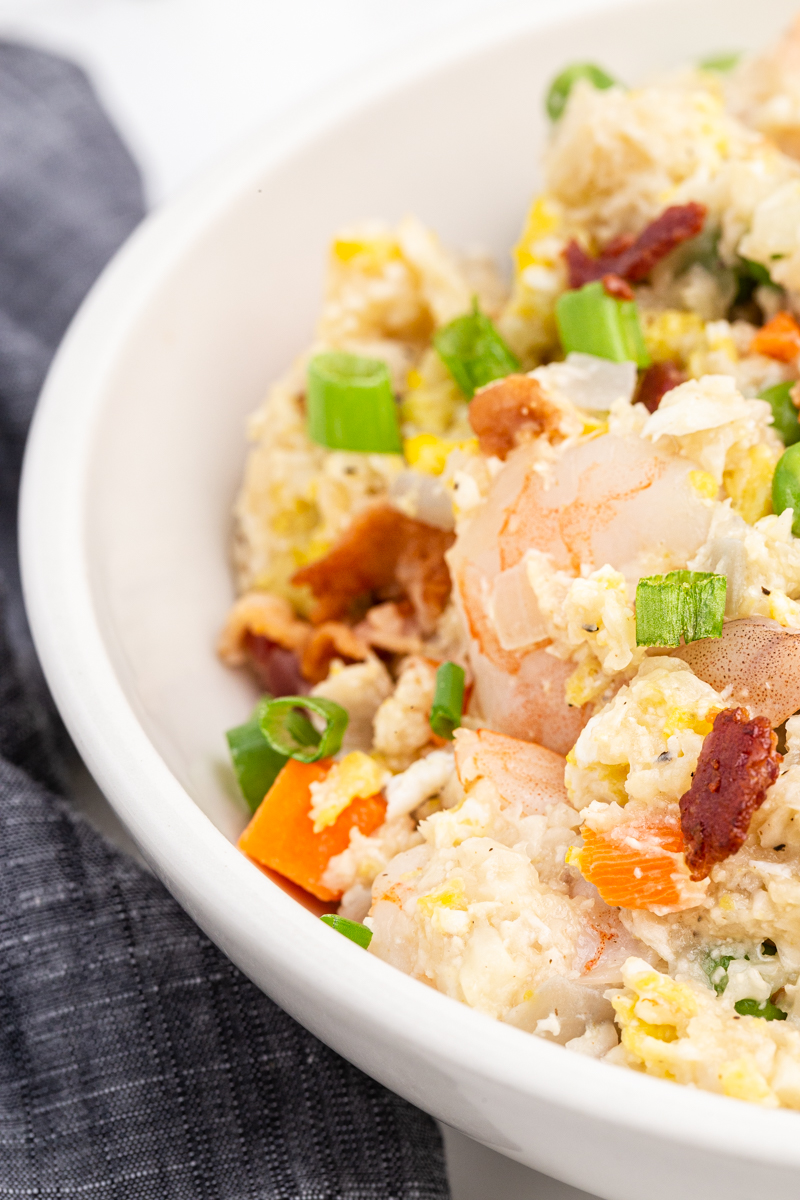 Extreme closeup of Shrimp Fried Cauliflower Rice with Bacon in a white bowl.