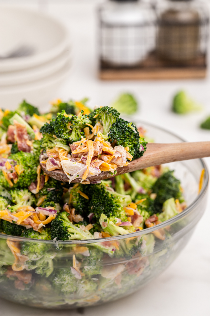 Close up photo of a spoonful of keto loaded broccoli salad over a full glass bowl of the salad.