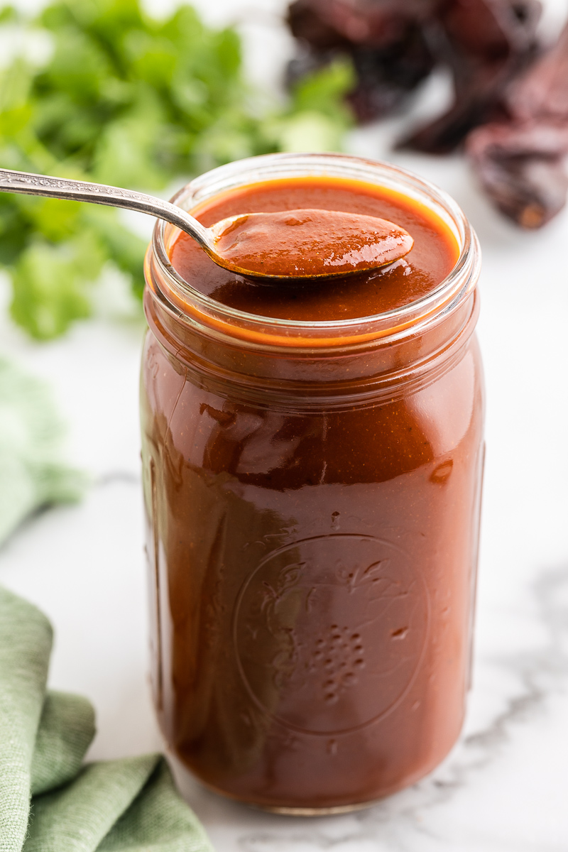 Photo of Homemade Red Enchilada Sauce in a mason jar with a spoon.
