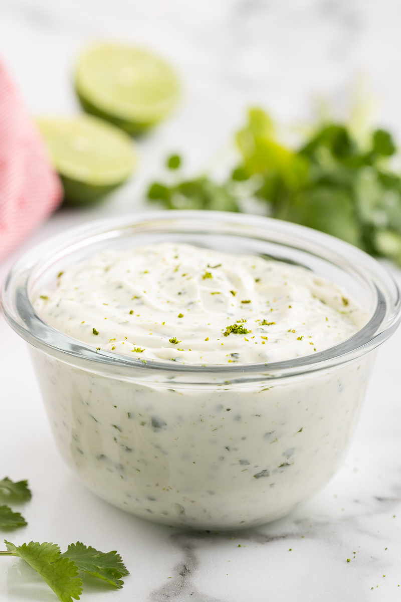 Close side view of Cilantro Lime Crema in a glass bowl on a white marble counter.
