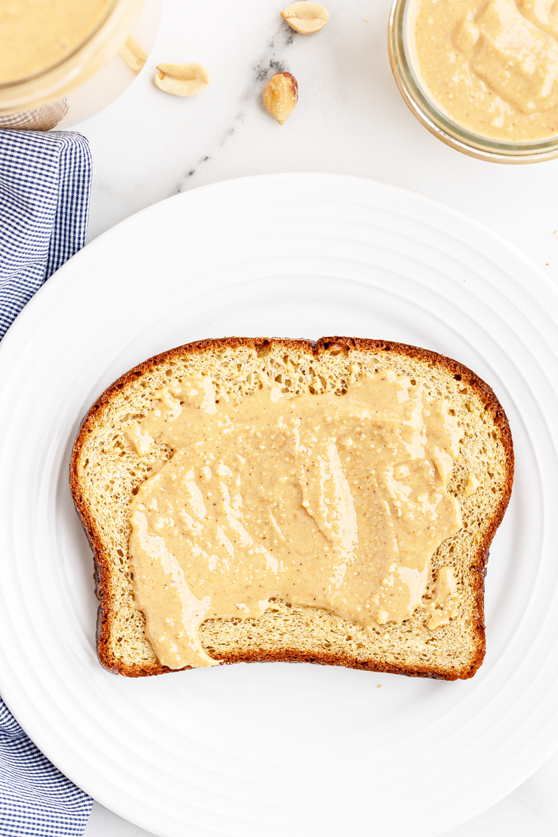 A slice of The BEST Keto Bread (Oven Method) with peanut butter on a white plate.