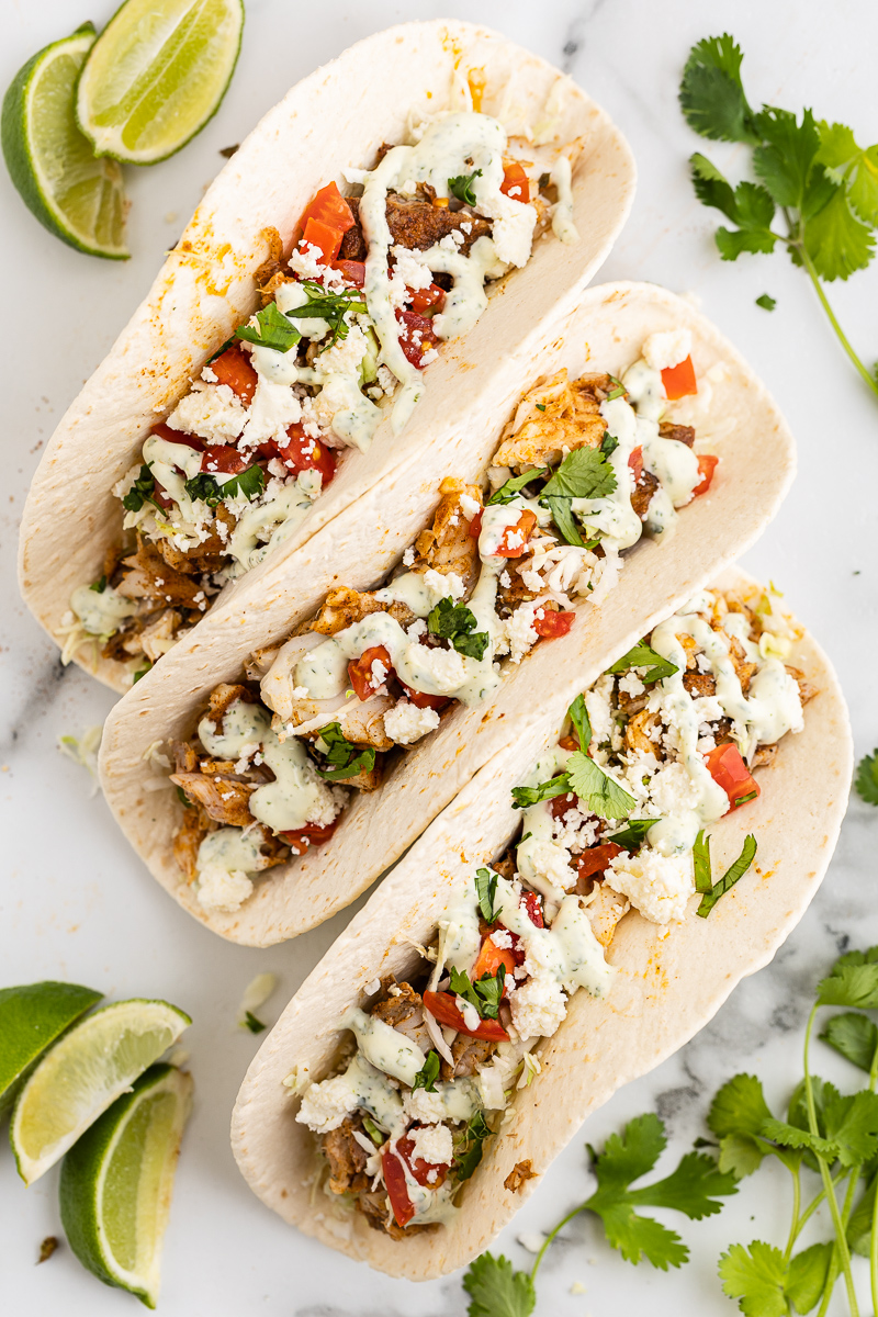 Overhead view of 3 Keto Fish Tacos on a white marble countertop with lime wedges scattered around.