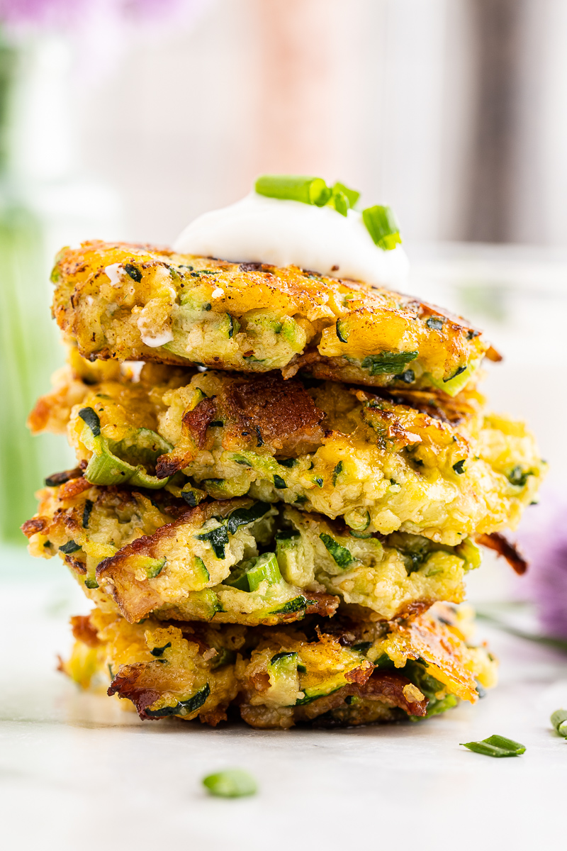 Close up photo of a stack of 4 Keto Cheesy Zucchini Fritters with Bacon on a white plate.