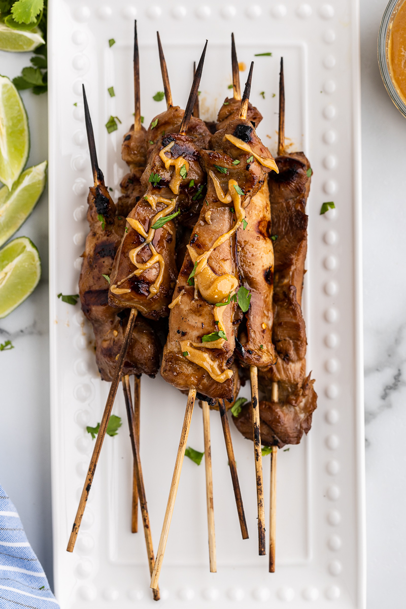 Overhead photo of several skewers of Chicken Satay with Spicy Peanut Sauce on a white serving platter.