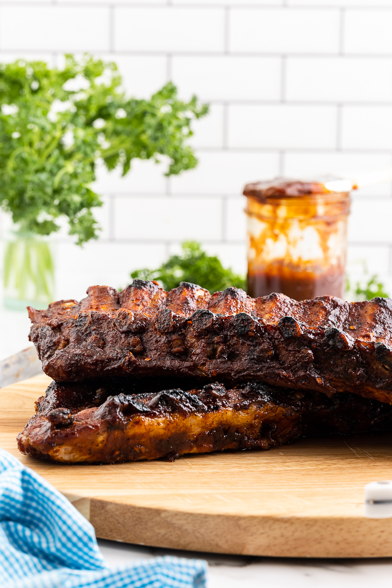 Keto BBQ ribs on a wooden cutting board with a jar of BBQ sauce in the background.