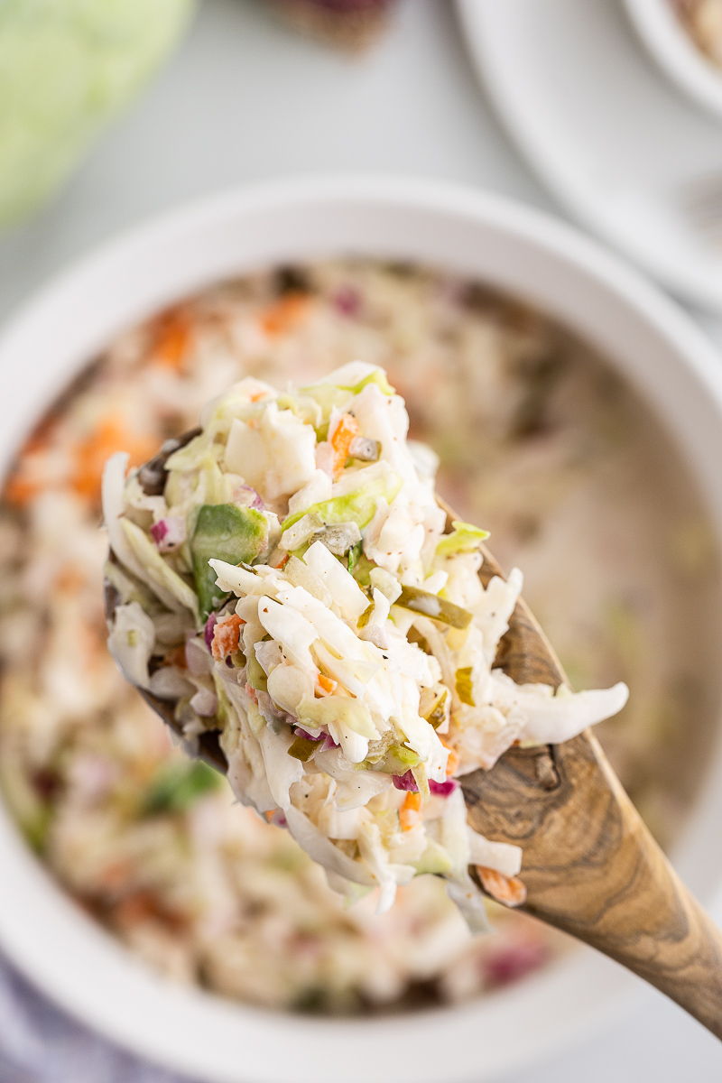 Overhead photo of a scoop of Dill Pickle Coleslaw on a serving spoon over the bowl full of coleslaw.