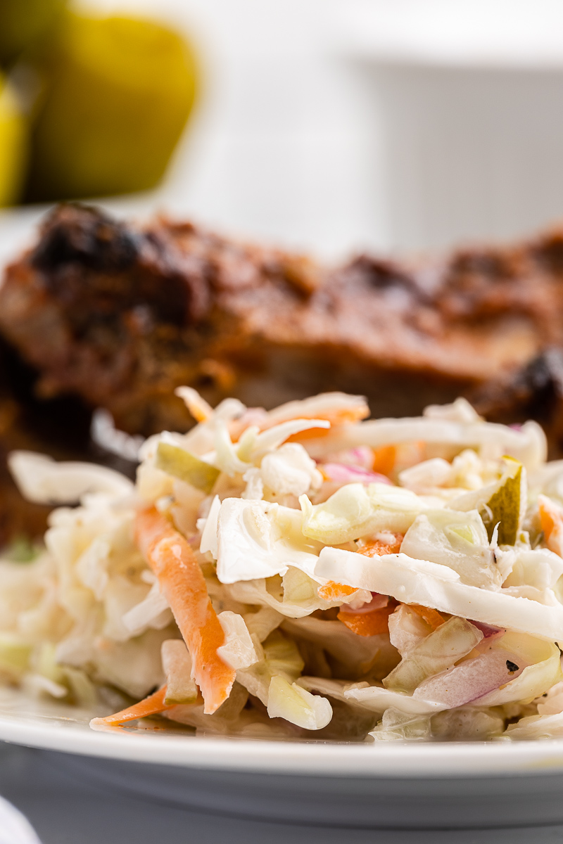 Extreme closeup of Dill Pickle Coleslaw on a white plate with BBQ ribs.