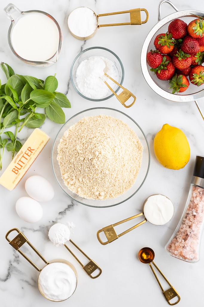 All of the ingredients needed to make keto strawberry basil shortcakes on a white marble counter.
