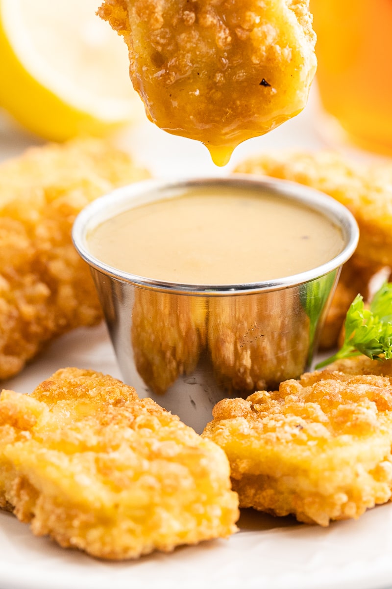 Closeup of a chicken nugget being dipped into sugar-free honey mustard sauce.