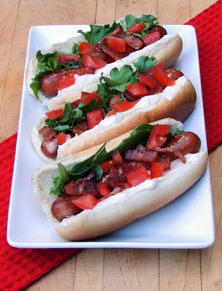 Three keto BLT hot dogs on a white serving tray with a red towel underneath it.