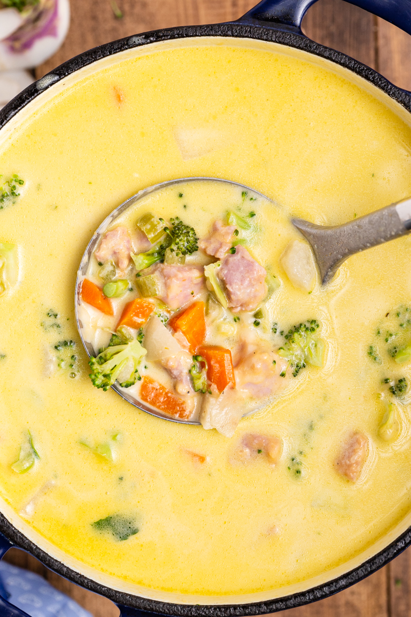 Overhead photo of Keto Cheesy Ham Chowder in a large blue pot with a ladle full closer to the camera.