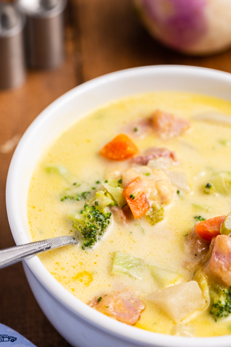Closeup photo of Keto Cheesy Ham Chowder in a white bowl on a wooden table.