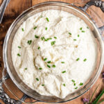 Roasted Garlic Mashed Cauliflower in a glass serving bowl with silver handles.