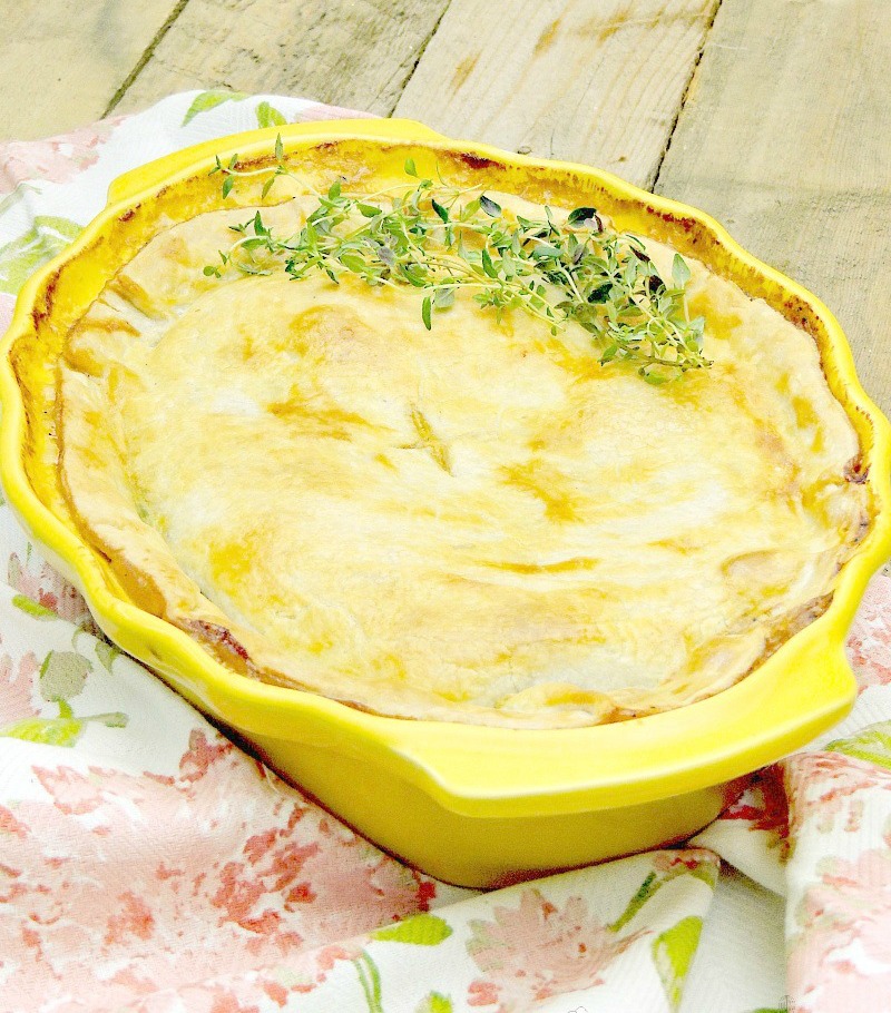 Salmon pot pie in a yellow casserole dish on a wooden table with floral towel.