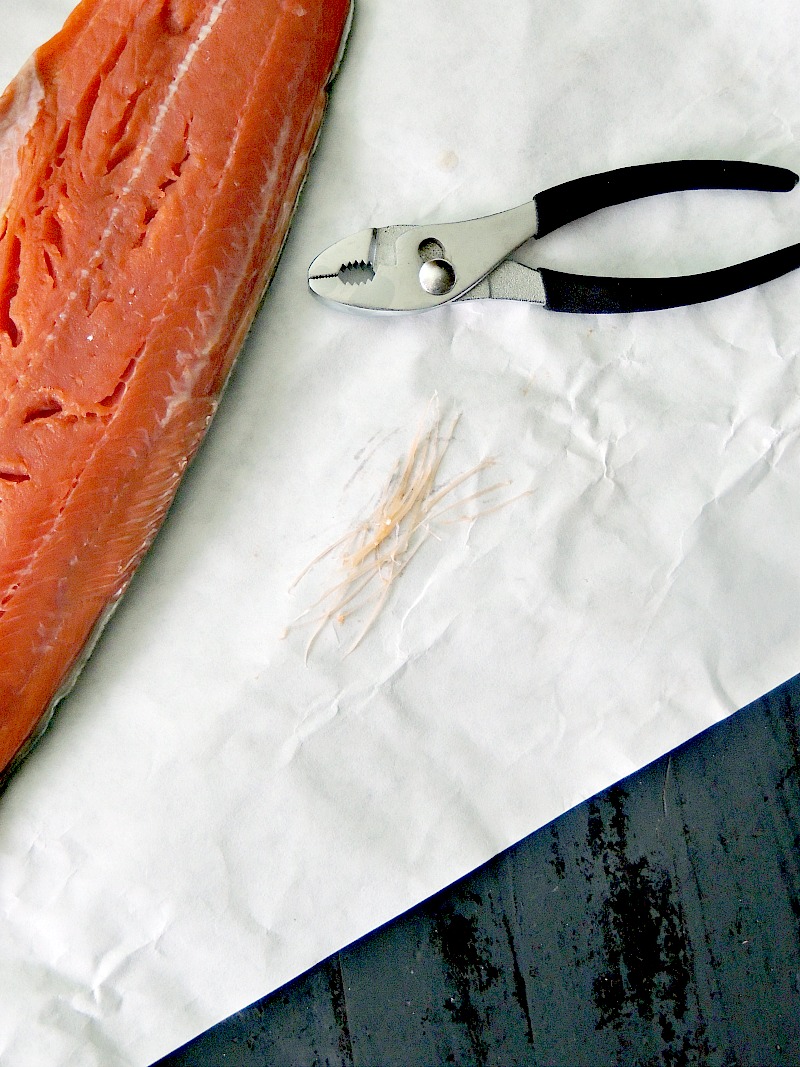 A salmon filet on butcher paper with a set of pliers and the pulled pin bones laying next to it.