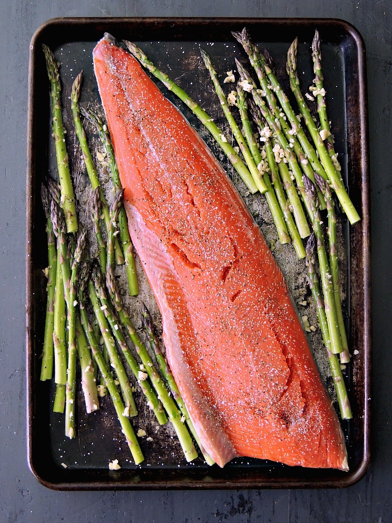 Overhead view of a salmon filet on top of asparagus spears on a sheet pan.