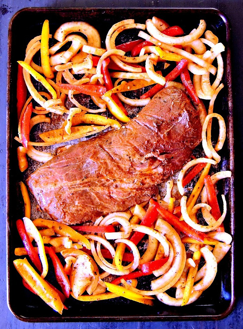 Overhead view of the marinated veggies and steak on the sheet pan getting ready to go into the oven.