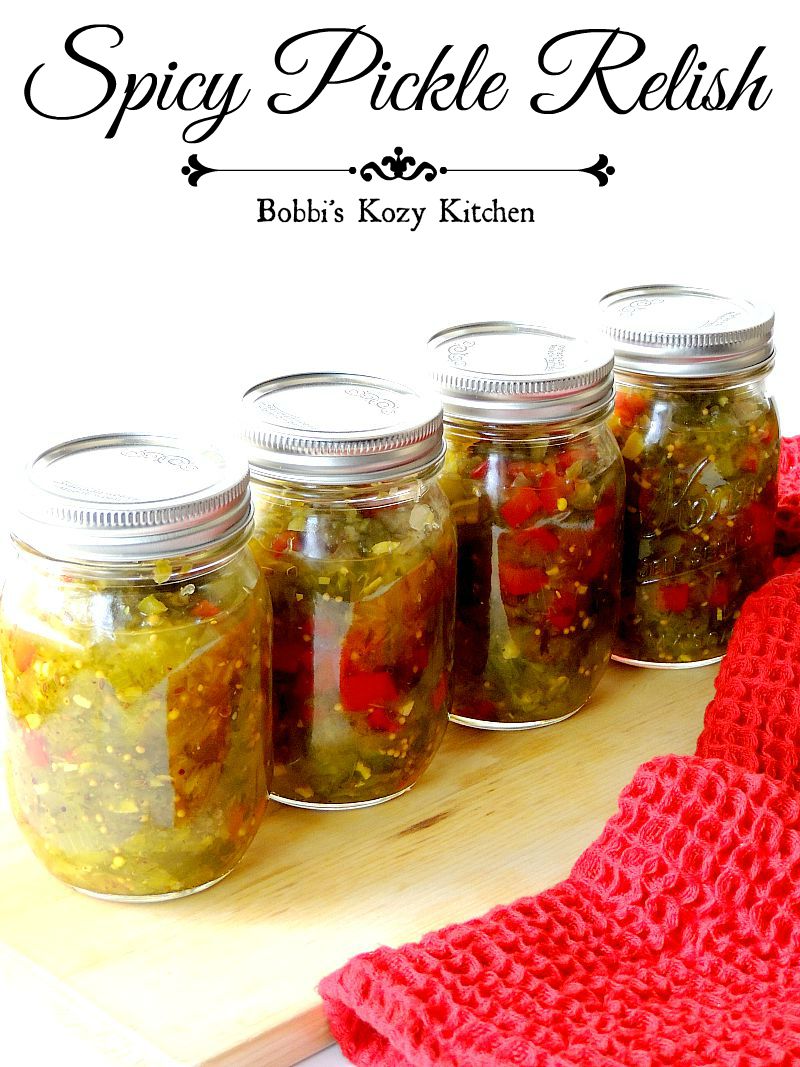 Four mason jars full of spicy pickle relish on a wooden cutting board with a red kitchen towel.