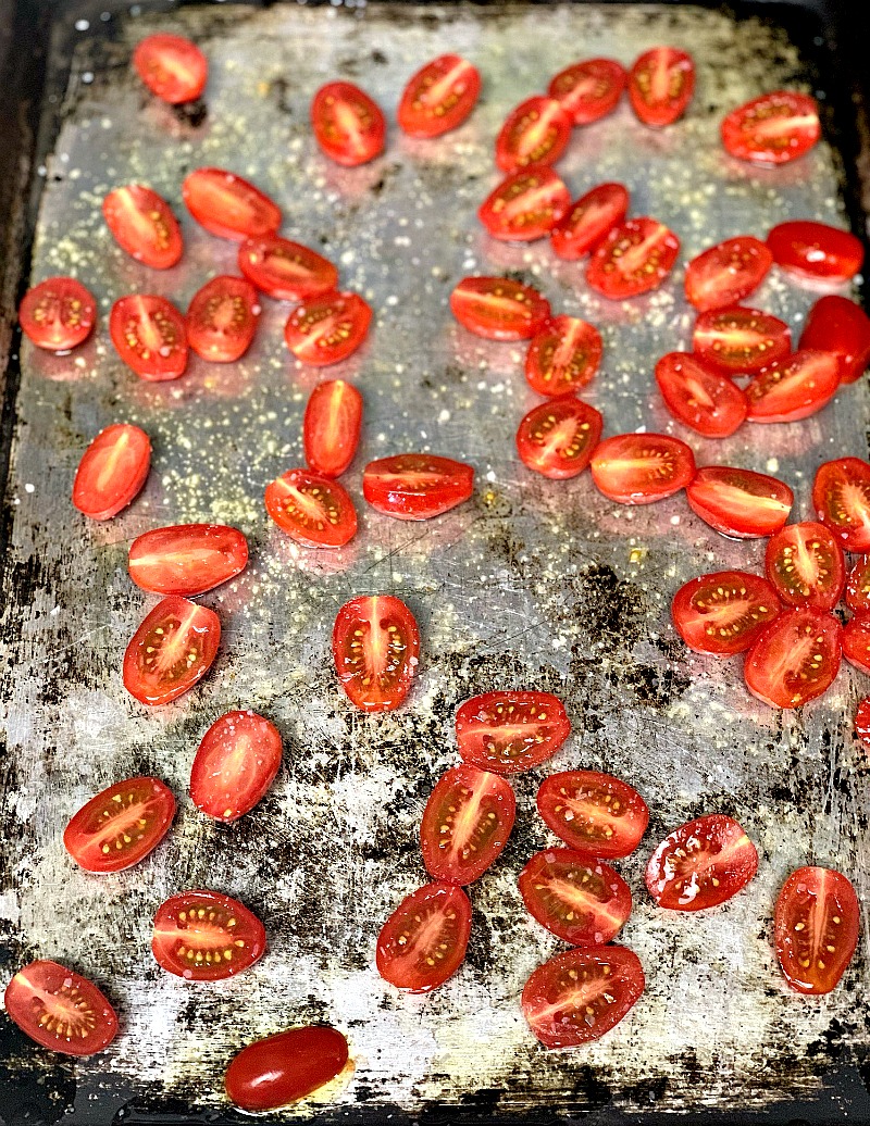 Fresh grape tomatoes halved and arranged in a single layer on a baking sheet, ready to be roasted in the oven for the BLT cauliflower salad recipe, with a sprinkle of olive oil, salt, and pepper for added flavor.