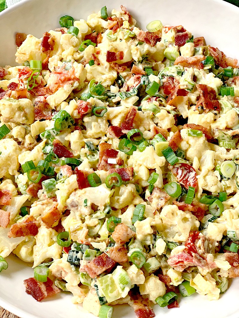 An extreme close-up view of the delicious BLT cauliflower salad in a white bowl, featuring crispy bacon, roasted grape tomatoes, sautéed leeks, chopped cauliflower florets, and fresh green onions, dressed with a creamy and tangy homemade sauce, a perfect low-carb and keto-friendly dish for a healthy and flavorful meal.