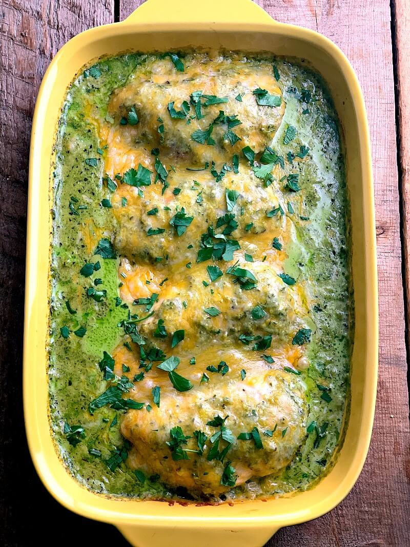 Overhead photo of Baked Green Chile Chicken in a yellow baking dish on a wooden table.
