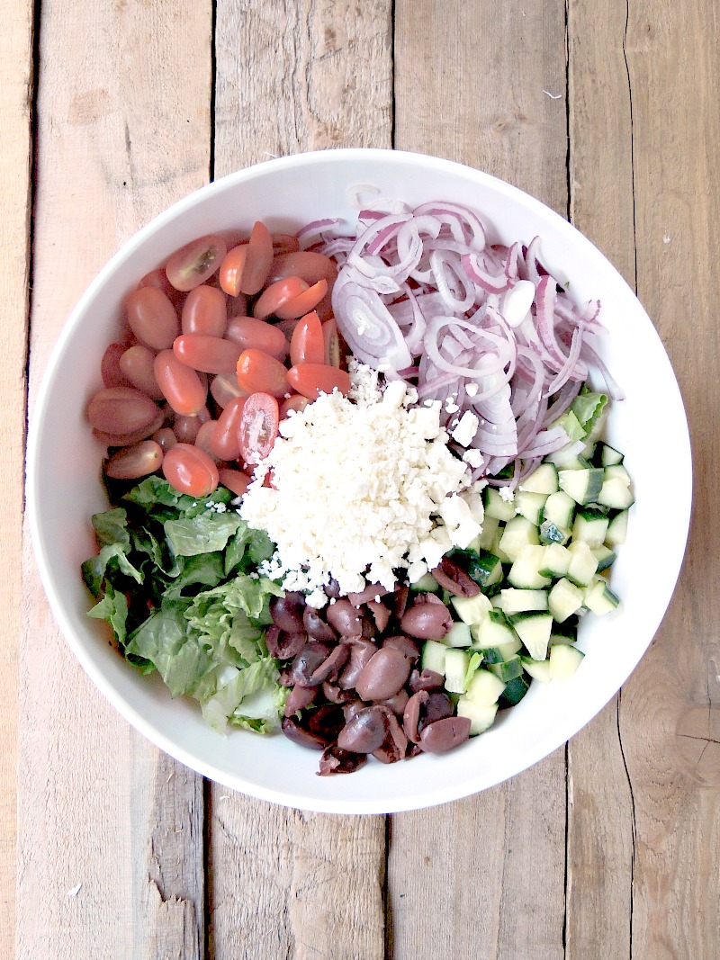 Overhead view of a large bowl full of the ingredients for the Greek Salad on a wooden table.