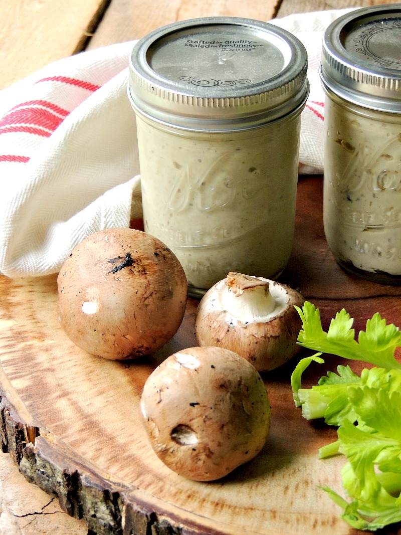 Two mason jars of Homemade Cream of Condensed Soup on a wooden cutting board with a few mushroom and celery leaves.