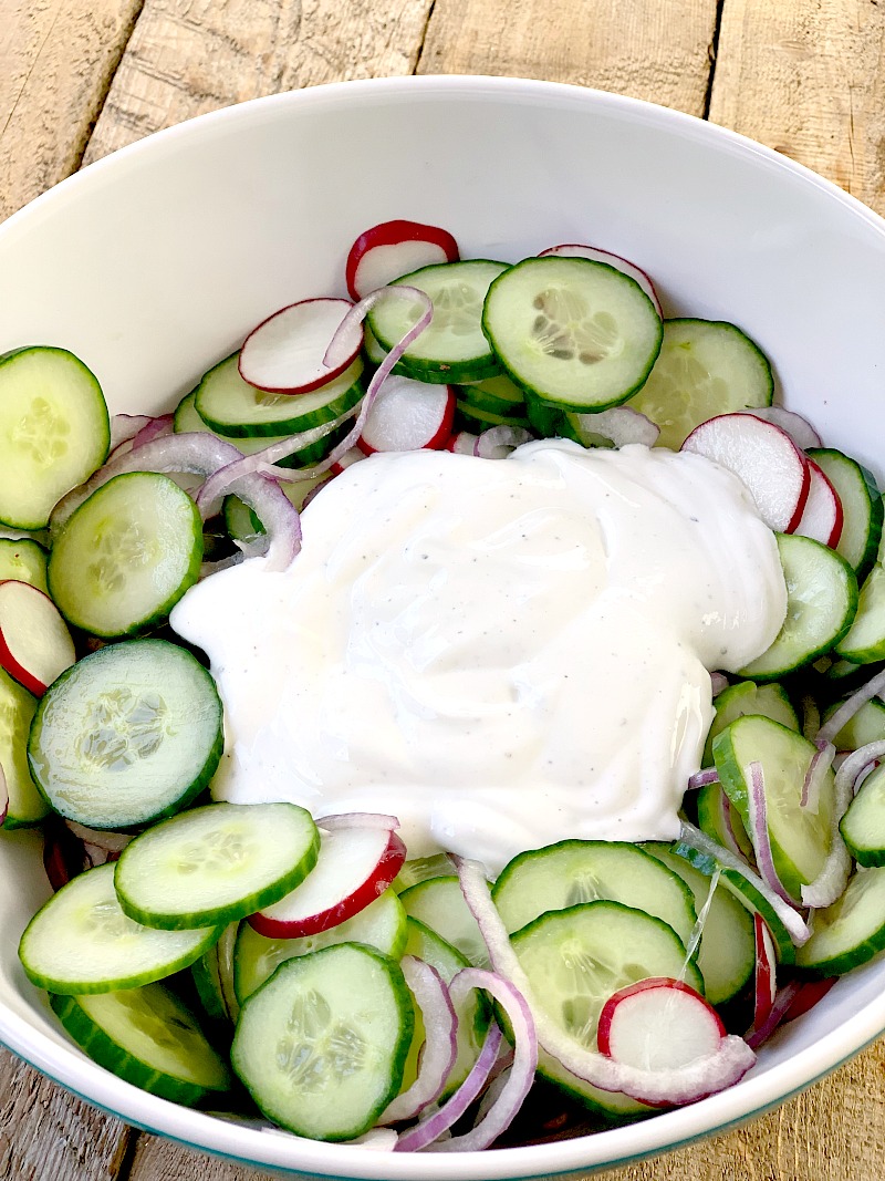 A large bowl with the sliced cucumbers, red onion, and radish in it with the creamy low carb sauce poured over the top. 