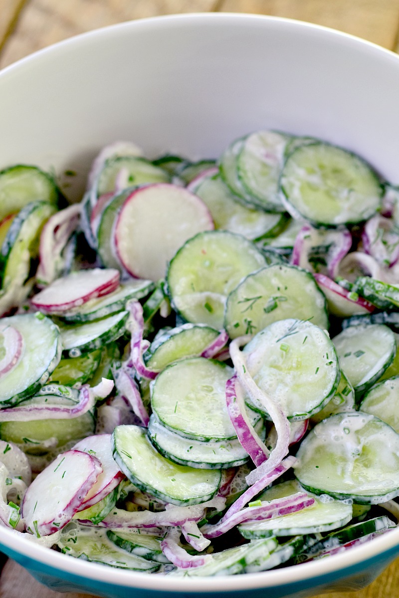 All of the ingredients to make Creamy Low Carb Cucumber Salad combined in a large bowl on a wooden table.