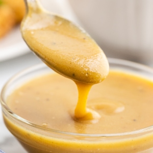 Closeup of a spoonful of keto honey mustard sauce over a glass bowl full of it.