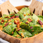 Spinach Salad with Hot Bacon and Tomato Vinaigrette in a wooden salad bowl.