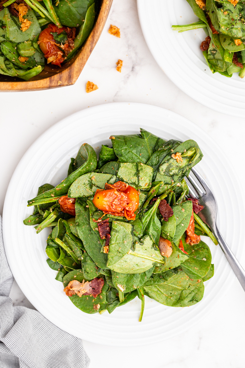 Overhead photo of Spinach Salad with Hot Bacon and Tomato Vinaigrette on a white salad plate.