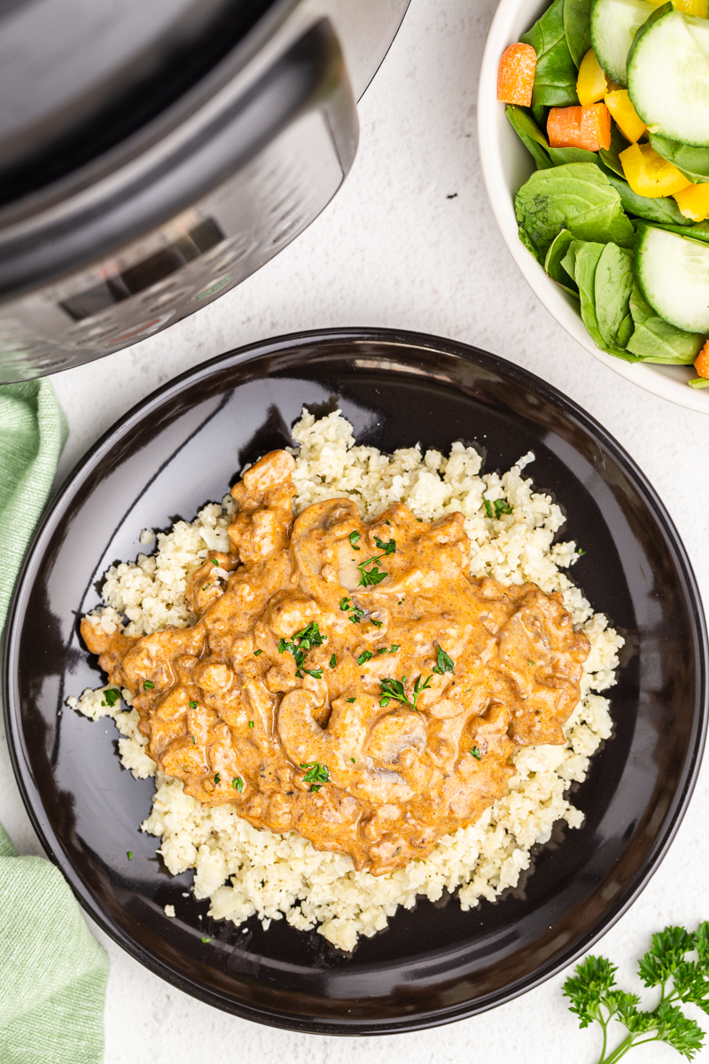 overhead view of keto ground beef stroganoff over cauliflower rice on a black dinner plate.