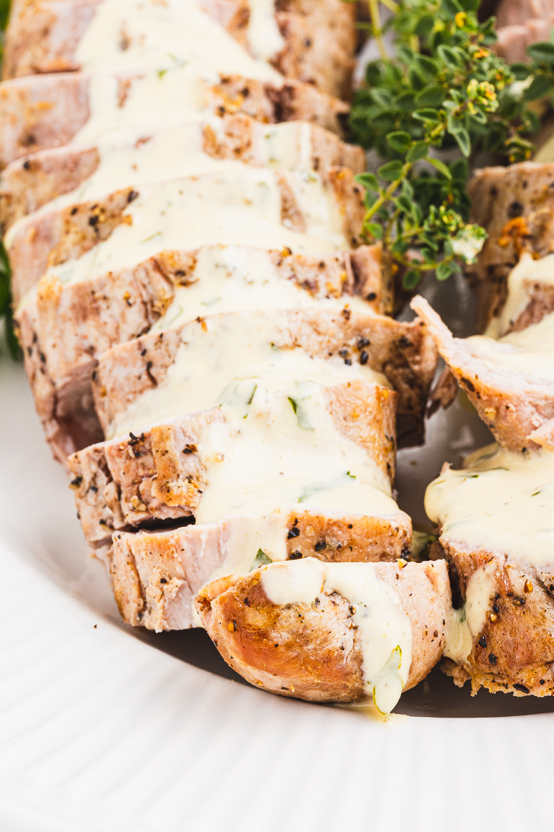 Closeup of Pork Tenderloin with Herb Mustard Sauce on a white serving platter.